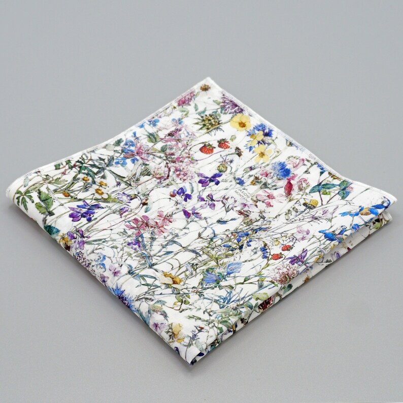 May include: A white cotton pocket square with a floral pattern featuring a variety of colorful wildflowers, including blue, purple, pink, yellow, and green.