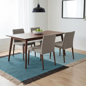May include: A rectangular wooden dining table with four upholstered chairs in a light gray fabric. The table and chairs are positioned on a large, textured area rug featuring a color-blocked pattern of teal and light blue with fringe edges.