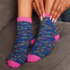 May include: A pair of blue socks with a colorful pattern and pink accents. The socks have a ribbed pink cuff and a pink heel and toe. The pattern includes lines of yellow, orange, green, and purple.