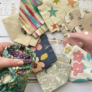 May include: A collection of small fabric pouches with various patterns, including stars, llamas, flowers, and stripes. The pouches are made of cotton fabric and have a zipper closure.