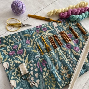 May include: A teal floral fabric roll-up case with a zipper closure and a strap. The case is filled with a variety of crochet hooks and a pair of gold scissors.