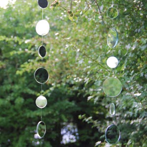 May include: A string of round, reflective, silver and clear glass ornaments hanging from a tree branch. The ornaments are suspended on a clear string.