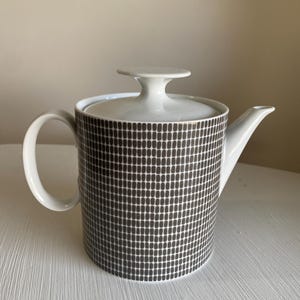 May include: White ceramic teapot with a lid and handle. The body features a pattern of small, dark brown rectangles. The spout and handle are white, and the lid has a small, round knob. A stylish tea accessory.