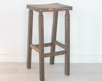 Tall bar chair with foot rest and made from reclaimed wood. Dark brown tall bar stool with foot rest and large seat.