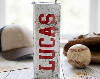 May include: A white and gray baseball-themed tumbler with the name "LUCAS" in red block letters. The tumbler has a silver straw and lid. A baseball, glove, and cap are in the background, suggesting a sports theme.