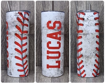 May include: A white stainless steel tumbler with a baseball design and the name "LUCAS" in red lettering. The tumbler has a red and white baseball stitch design.