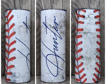 May include: White stainless steel tumbler with a baseball stitch design and a blue signature that says "Hunter".