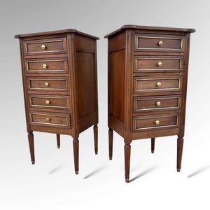 May include: A pair of antique wooden bedside cabinets. Each cabinet features six drawers with gold trim and gold knobs. The cabinets have slender legs and a dark brown finish. The cabinets are displayed against a white background.