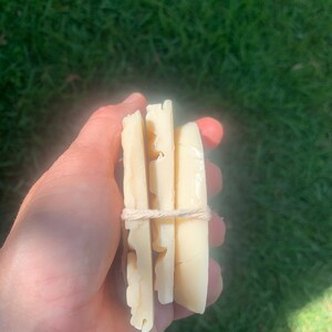 May include: Three bars of white soap wrapped with twine. The soap is rectangular and has a textured surface.