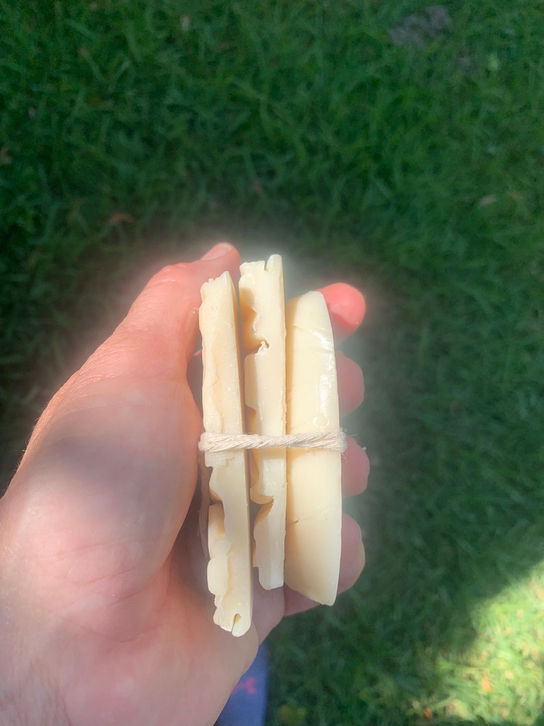 May include: Three bars of white soap wrapped with twine. The soap is rectangular and has a textured surface.