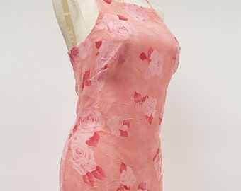 May include: A floor-length, coral-colored dress with a floral rose pattern. The dress features a square neckline and spaghetti straps. The fabric has a textured appearance, and the roses are in shades of pink and red.