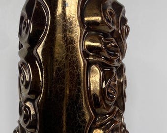 Könnte beinhalten: Eine hohe, bronzefarbene Keramikvase mit strukturierter Oberfläche und aufwendigen Reliefmustern. Die Vase hat eine zylindrische Form mit ausgestelltem Fuß und einer breiten Öffnung oben. Das Reliefdesign zeigt wirbelnde, organische Formen.