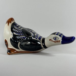 May include: A ceramic duck figurine with a white body, black wings, and blue and brown accents. The duck has a blue beak and is designed with intricate patterns. The figurine is a decorative item.