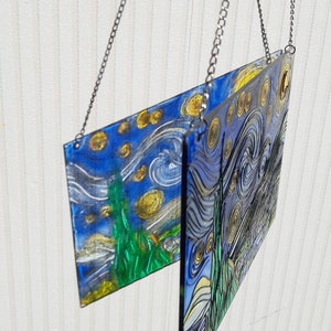 May include: Two glass panels with a painting of Van Gogh's Starry Night hanging from a silver chain. The panels are slightly offset from each other, creating a unique visual effect.