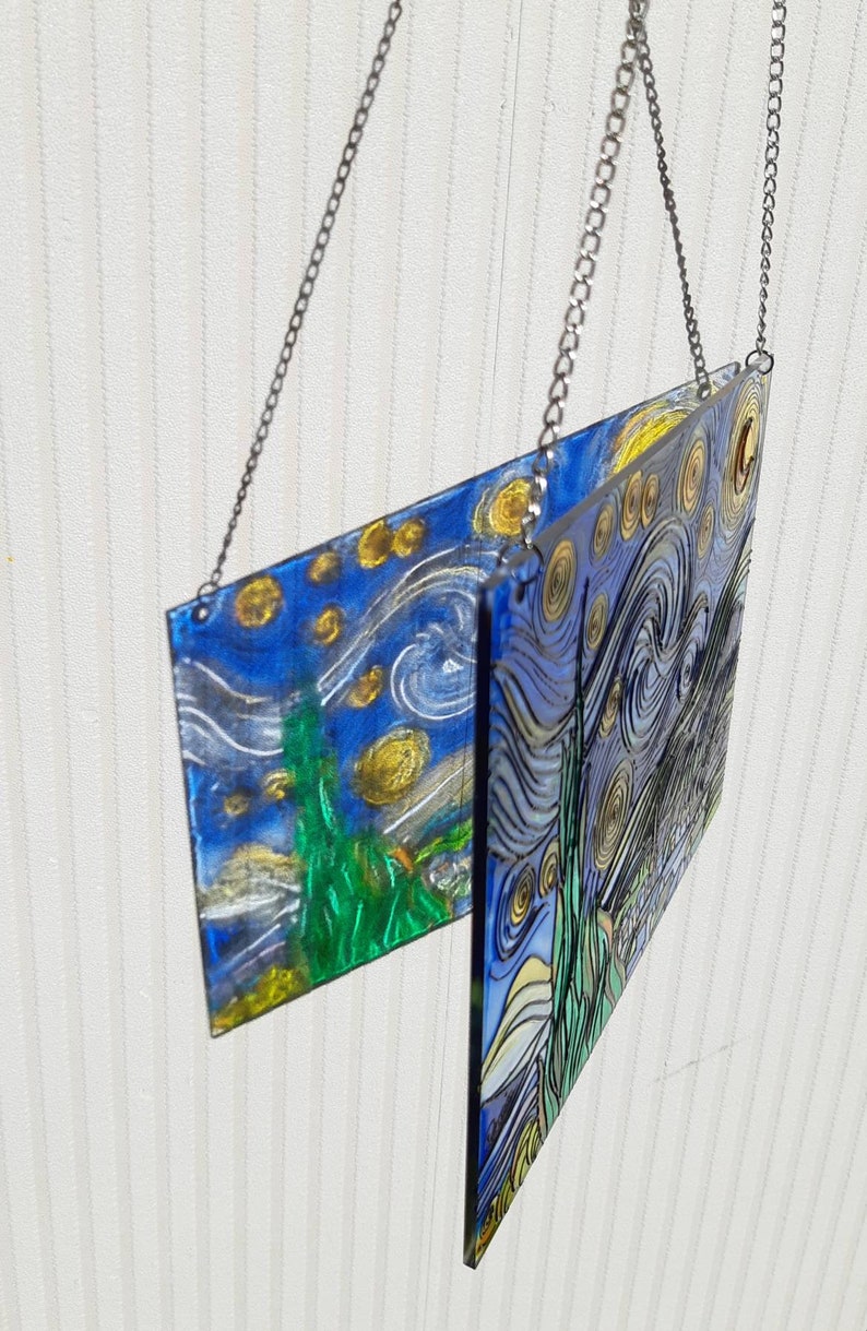 May include: Two glass panels with a painting of Van Gogh's Starry Night hanging from a silver chain. The panels are slightly offset from each other, creating a unique visual effect.