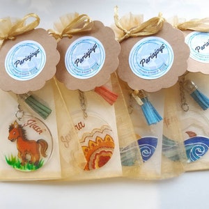 Op de afbeelding: Vier transparante acryl sleutelhangers met verschillende ontwerpen en namen. De sleutelhangers zijn verpakt in individuele organza zakjes met een bruin label waarop "Pariajoys Craft Shop & Gift" staat. De ontwerpen omvatten een paard, een mandala en twee oceaan golven.