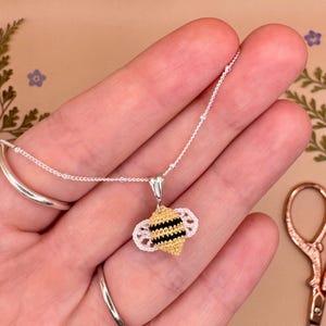 May include: A silver chain necklace with a crocheted bee pendant. The bee is yellow and black with white wings.
