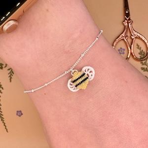 May include: A silver chain bracelet with a crocheted bee charm. The bee is yellow and black with white wings.