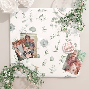 May include: A white fabric-covered bulletin board with a botanical print of green leaves and flowers. Two family photos and a button that says "I'm the sister of someone who's talented, charming, and delightful" are attached to the board.