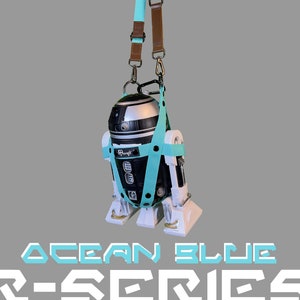 May include: A teal blue and black R-Series robot with a white base and a brown and teal blue strap. The robot is hanging from the strap. The text "OCEAN BLUE R-SERIES" is printed below the robot.