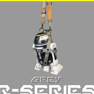 May include: A grey R-Series robot with a black and silver body is suspended by a brown and black strap. The robot has a white base and is labeled "GREY R-SERIES".