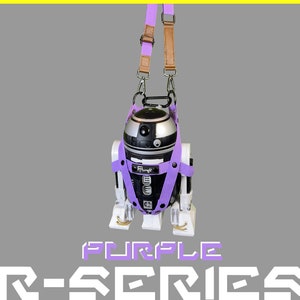May include: A purple R-Series robot with a black and silver body, hanging from a brown and purple strap. The robot has a black and white face with the word "Flungff" printed on it. The strap is attached to the robot's head and shoulders.