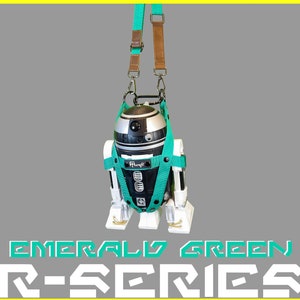May include: A teal green and black R2-D2 robot with a brown and teal green strap. The robot is hanging from the strap. The text "EMERALD GREEN R-SERIES" is at the bottom of the image.