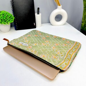 May include: A green laptop sleeve with a floral pattern and a zipper closure. The sleeve has a label that says "ART-9802".