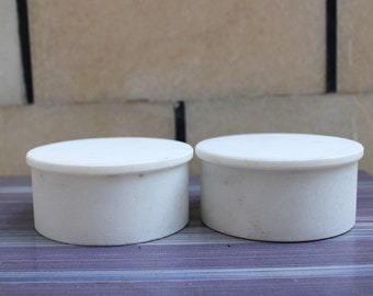 May include: Two white round ceramic containers with smooth surfaces. The containers are similar in size and shape.