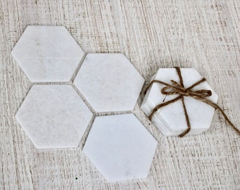 May include: Set of six white hexagon-shaped coasters made of marble. The coasters are tied together with twine.