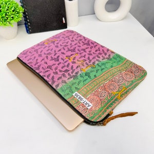 Op de afbeelding: Een laptoptas met een bloemenpatroon in roze en groen. De hoes heeft een zwarte rits en een bruine leren trekker. Een laptop is gedeeltelijk ingevoegd. Het label luidt ART-9836.