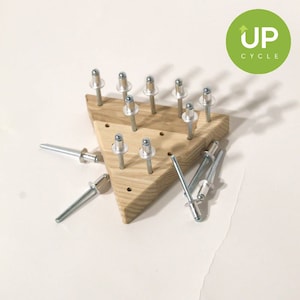 May include: A wooden triangle with holes and silver metal rivets. The rivets are scattered around the triangle, some are in the holes and some are loose.