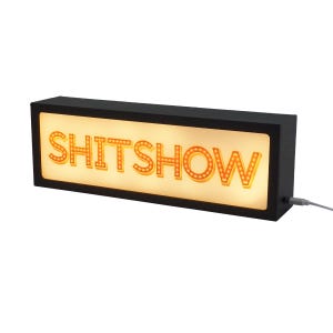 以下が含まれることがあります： 「SHITSHOW」の文字がオレンジ色に光る、長方形の黒いライトボックス。文字は小さな丸いライトで縁取られています。USBケーブルがボックスの側面から出ています。