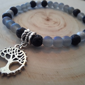 May include: A grey and black beaded bracelet with a silver tree of life charm. The bracelet is made with lava rock and frosted glass beads.