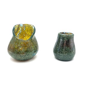 May include: Two glass vases with a speckled green and blue finish. The larger vase has a wider opening and a yellow and blue swirl inside. The smaller vase has a narrower opening and a darker green and blue swirl inside.