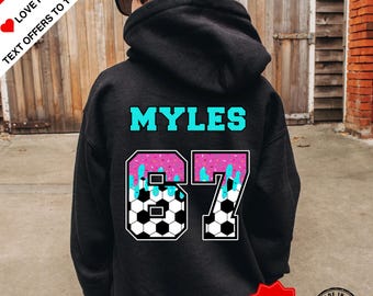 May include: Black hoodie with the name "MYLES" in turquoise letters. The number "67" is designed with a soccer ball pattern and pink and blue frosting. The hoodie has "SPECIAL GIFT" and "MADE IN U.S.A." labels.