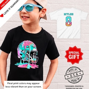 May include: A black t-shirt featuring a colorful graphic of a football helmet with a donut design. The image also shows a white t-shirt with the name "MYLES" and the number "8". Additional text includes "Final print colors may appear less vibrant than on your screen."