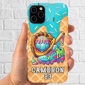 May include: A phone case featuring a baseball theme with a colorful, cartoonish design. The case has a waffle cone pattern background with a baseball glove, bat, and shoe. The name "CAMERON" and the number "23" are displayed.