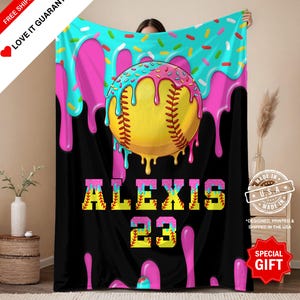 Könnte beinhalten: Eine schwarze Decke mit einem Softball-Design. Sie zeigt einen gelben Ball mit rosa und blauen Zuckerguss, den Namen "ALEXIS" und die Nummer "23". Die Decke hat ein "SPECIAL GIFT"-Etikett und ein "MADE IN U.S.A."-Siegel.