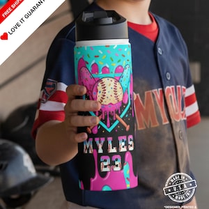 May include: A baseball-themed water bottle with a black lid and a colorful design. The design includes a baseball, bats, and the name "MYLES" with the number "23". The bottle has a teal top with sprinkles and pink accents.