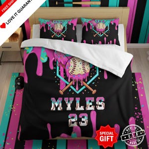 May include: A black and pink baseball-themed bedding set with a baseball graphic and the name "MYLES 23". The set includes a comforter, two pillowcases, and a matching rug. The design features a baseball with dripping pink frosting and crossed bats.