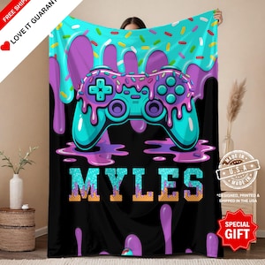May include: A black blanket featuring a teal and purple video game controller design with a donut-themed background. The name "MYLES" is displayed in teal and gold letters. The blanket is designed, printed, and shipped in the USA.