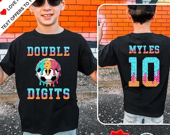 Könnte beinhalten: Schwarzes T-Shirt mit dem Text "DOUBLE DIGITS" und einem Fussball-Design mit einem bunten, donutartigen Muster. Auf der Rückseite des Shirts steht "MYLES 10". Hergestellt in den USA.
