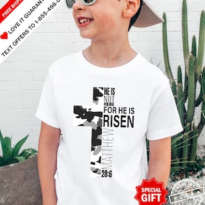 May include: White t-shirt featuring a camouflage cross design with the text "HE IS NOT HERE FOR HE IS RISEN" and "MATTHEW 28:6". The shirt has a crew neck and short sleeves. The image also includes text offering a guarantee and special gift.