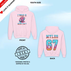 May include: Pink youth-sized hoodie with a front graphic that reads "I WAS 6, NOW I'M 7" and a football design. The back of the hoodie displays "MYLES 67". The hoodie is made in the USA.