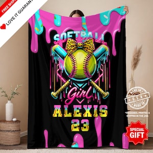 Könnte beinhalten: Schwarze Softball-Decke mit einem lebendigen Design. Verfügt über einen gelben Softball mit Leopardenmuster-Schleife, gekreuzten Schlägern und dem Text "Softball Girl Alexis 23". Die Oberseite hat rosa und blaue tropfende Farbe.