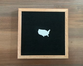 May include: A black felt letter board with a white outline of the United States of America.