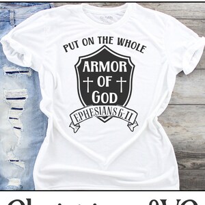 May include: White t-shirt with black text that reads "Put on the whole armor of God Ephesians 6:11". The text is in a shield shape with a cross on each side.