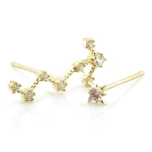 May include: A pair of gold earrings featuring a constellation design with small clear and pink gemstones. The earrings are made of gold and have a delicate, feminine look.