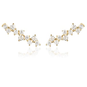 May include: A pair of gold earrings with a curved design featuring a cluster of small, clear cubic zirconia stones.